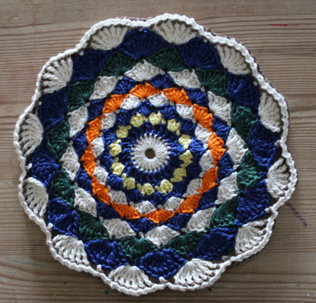 hæklet cirkel i muslingemønster - 22,5 cm i diameter - blå-gul-orange-grøn med brun kant