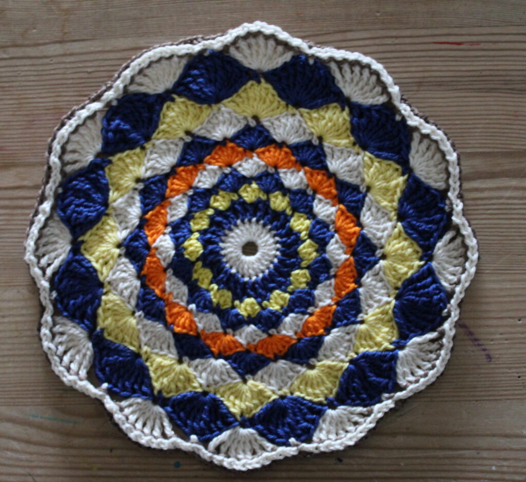 hæklet cirkel i muslingemønster - 22,5 cm i diameter - blå-gul-orange med brun kant