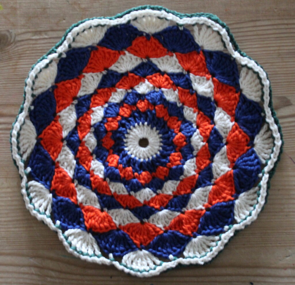 hæklet cirkel i muslingemønster - 22,5 cm i diameter - blå-orange med grøn kant